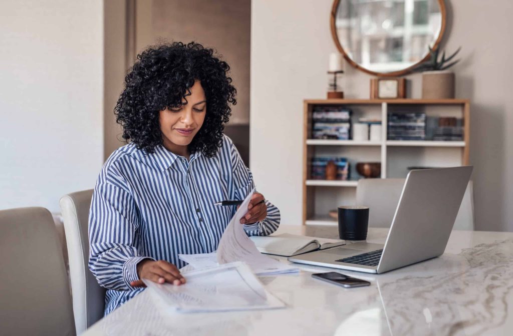 Woman reviewing paperwork at a table with a laptop