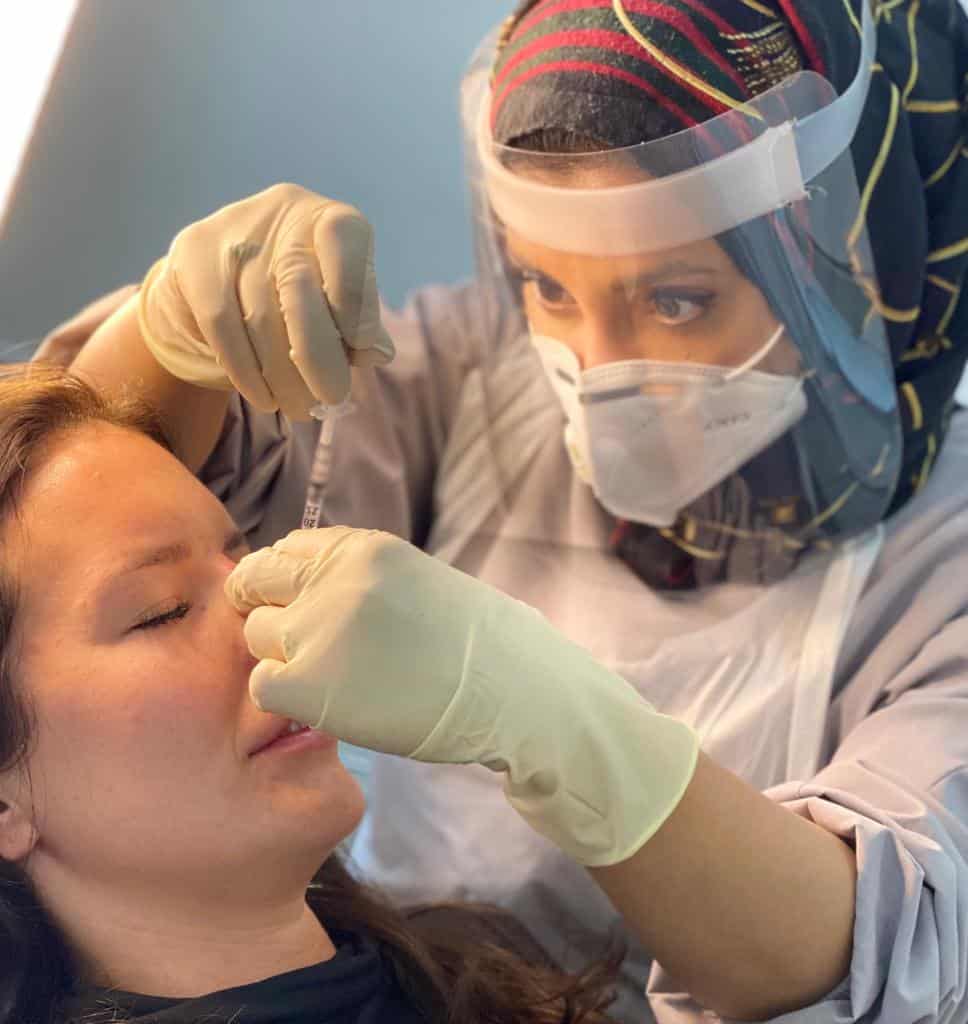 Practitioner in a face shield and mask performing a facial injection