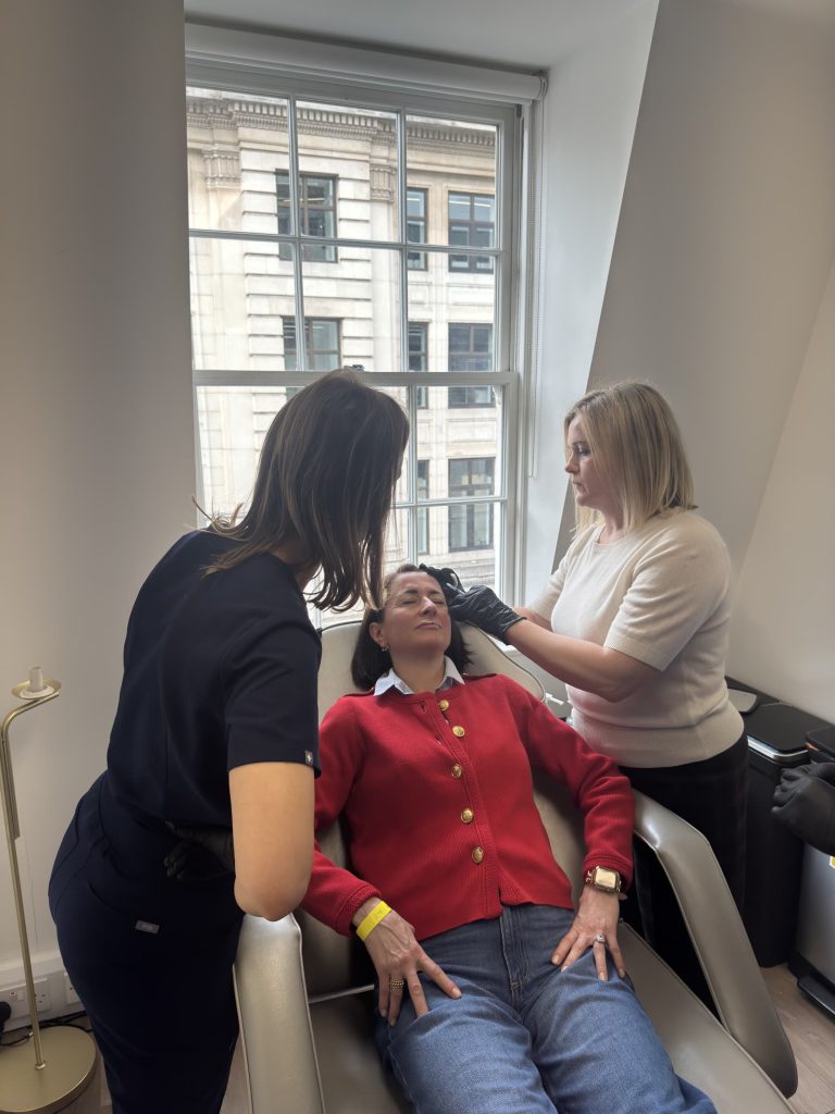 Two practitioners assess a model patient's face before treatment during a supervised session.